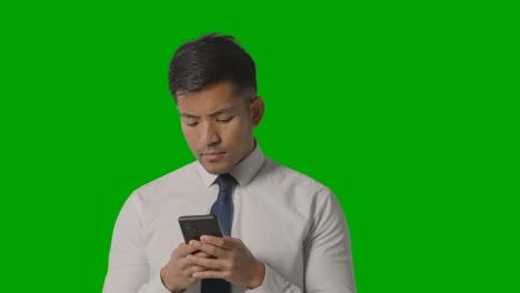 Studio-Shot-Of-Serious-Businessman-In-Shirt-And-Tie-Using-Mobile-Phone-Against-Green-Screen-