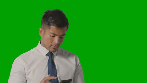 Studio-Shot-Of-Businessman-In-Shirt-And-Tie-Thinking-Using-Mobile-Phone-Against-Green-Screen-