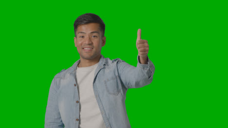 Studio-Shot-Of-Casually-Dressed-Young-Man-Giving-Thumbs-Up-Gesture-Against-Green-Screen-