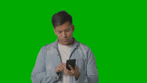 Studio-Shot-Of-Casually-Dressed-Young-Man-Online-Swiping-On-Mobile-Phone-Against-Green-Screen-2