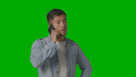 Studio-Shot-Of-Casually-Dressed-Serious-Young-Man-Talking-On-Mobile-Phone-Against-Green-Screen-