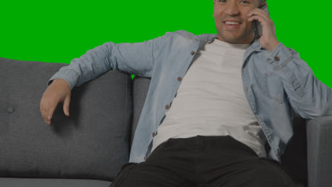 Close-Up-Of-Young-Man-Sitting-On-Sofa-Talking-On-Mobile-Phone-Against-Green-Screen-
