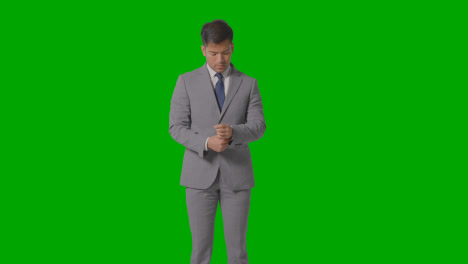 Three-Quarter-Length-Portrait-Of-Businessman-In-Suit-Straightening-Cuffs-Against-Green-Screen-
