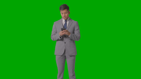 Three-Quarter-Length-Studio-Shot-Of-Businessman-In-Suit-Looking-At-Mobile-Phone-Against-Green-Screen-2