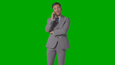 Three-Quarter-Length-Studio-Shot-Of-Smiling-Businessman-In-Suit-Talking-On-Mobile-Phone-Against-Green-Screen-1