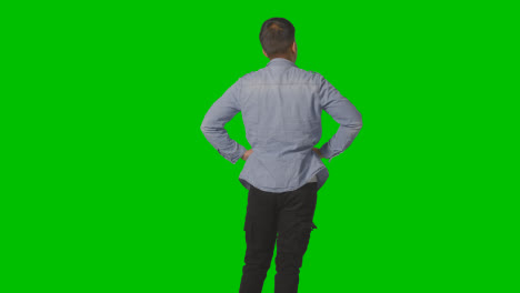 Three-Quarter-Length-Studio-Rear-View-Of-Casually-Dressed-Young-Man-Looking-At-Green-Screen-
