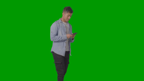 Studio-Shot-Of-Casually-Dressed-Young-Man-Checking-Mobile-Phone-Against-Green-Screen-1