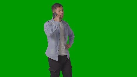Studio-Shot-Of-Casually-Dressed-Young-Man-Talking-On-Mobile-Phone-Against-Green-Screen-