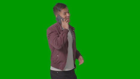 Studio-Shot-Of-Smiling-Casually-Dressed-Young-Man-Talking-On-Mobile-Phone-Against-Green-Screen-