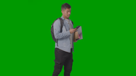 Three-Quarter-Length-Shot-Of-Male-University-Or-College-Student-Looking-At-Mobile-Phone-Against-Green-Screen-1