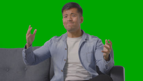 Studio-Shot-Of-Disappointed-Young-Man-Sitting-On-Sofa-Watching-Sport-On-TV-Against-Green-Screen-2