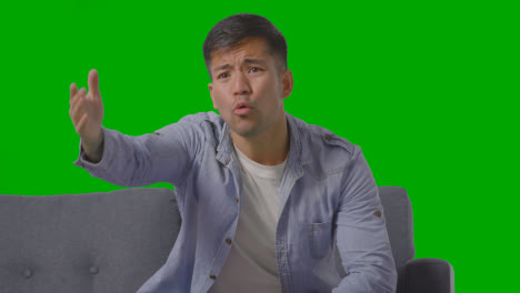 Studio-Shot-Of-Disappointed-Young-Man-Sitting-On-Sofa-Watching-Sport-On-TV-Against-Green-Screen-3