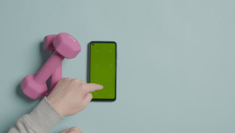 Foto-De-Estudio-De-Fitness-Superior-De-Pesas-Con-Mancuernas-De-Ejercicio-Con-La-Mano-Usando-El-Teléfono-Móvil-De-Pantalla-Verde-2