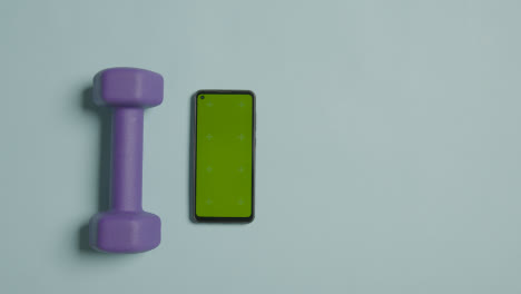 Overhead-Fitness-Studio-Shot-Of-Male-Hand-Picking-Up-Exercise-Dumbbell-Weights-Next-To-Green-Screen-Mobile-Phone-3