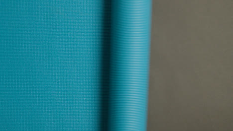 Full-Frame-Shot-Of-Blue-Exercise-Mat-Being-Rolled-Across-Frame-Before-Fitness-Class