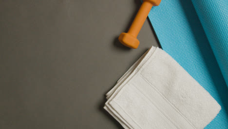 Overhead-Fitness-Studio-Shot-Of-Male-Hand-Picking-Up-Water-Bottle-With-Exercise-Weights-Mat-And-Towel