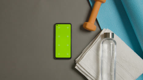 Overhead-Fitness-Studio-Shot-Of-Male-Hand-Picking-Up-And-Throwing-Down-Water-Bottle-Next-To-Green-Screen-Mobile-Phone