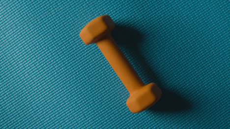 Overhead-Studio-Fitness-Shot-Of-Rotating-Yellow-Hand-Weight-On-Blue-Exercise-Mat-1