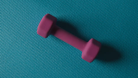 Overhead-Studio-Fitness-Shot-Of-Rotating-Pink-Hand-Weight-On-Blue-Exercise-Mat
