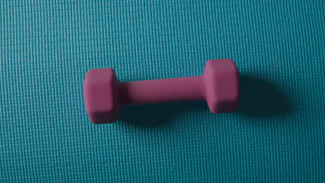 Overhead-Studio-Fitness-Shot-Of-Rotating-Pink-Hand-Weight-On-Blue-Exercise-Mat-With-Lighting-Fading-Up-And-Down