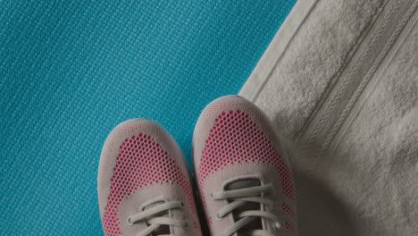 Overhead-Studio-Fitness-Shot-Of-Rotating-Trainers-With-Towel-On-Blue-Exercise-Mat-With-Lighting-Fading-Up-And-Down