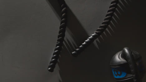 Overhead-Studio-Fitness-Shot-Of-Battle-Rope-On-Grey-Background-With-Hand-Picking-Up-Gym-Weight