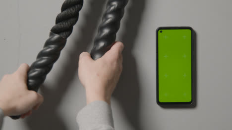 Overhead-Studio-Fitness-Shot-Of-Hands-Picking-Up-Gym-Battle-Ropes-With-Green-Screen-Mobile-Phone-On-Grey-Background