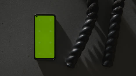 Overhead-Studio-Fitness-Shot-Of-Hands-Picking-Up-Gym-Battle-Ropes-With-Green-Screen-Mobile-Phone-On-Grey-Background-3