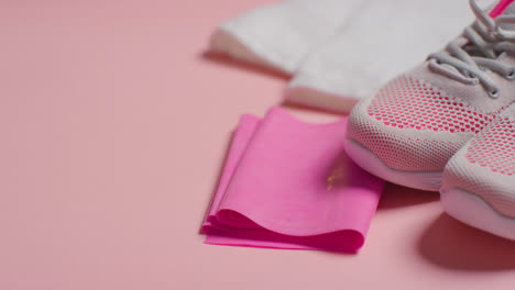 Close-Up-Studio-Fitness-Shot-Of-Trainers-With-Resistance-Band-And-Towel-On-Pink-Background