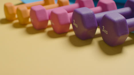 Studio-Fitness-Shot-Showing-Colourful-Gym-Weights-In-A-Line-On-Yellow-Background
