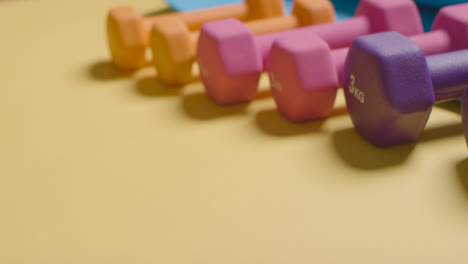 Studio-Fitness-Shot-With-Hand-Putting-Down-Colourful-Gym-Weights-In-A-Line-On-Yellow-Background-1