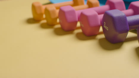 Foto-De-Fitness-De-Estudio-Con-La-Mano-Colocando-Pesas-De-Gimnasio-Coloridas-En-Una-Línea-Sobre-Fondo-Amarillo-1