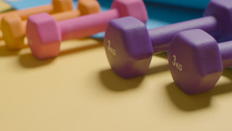 Studio-Fitness-Shot-With-Hand-Picking-Up-Colourful-Gym-Weights-In-A-Line-On-Yellow-Background-1