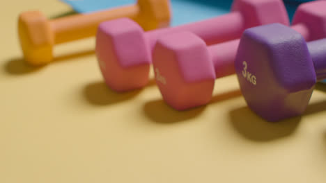 Studio-Fitness-Shot-With-Hand-Picking-Up-Colourful-Gym-Weights-In-A-Line-On-Yellow-Background-2