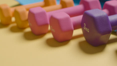 Studio-Fitness-Shot-With-Hand-Putting-Down-Colourful-Gym-Weights-In-A-Line-On-Yellow-Background-2