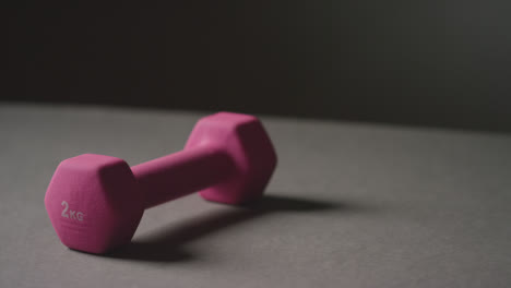 Close-Up-Studio-Fitness-Shot-Of-Hand-Picking-Up-Pink-Gym-Weight-On-Grey-Background