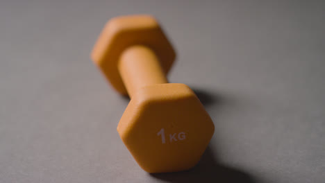 Close-Up-Studio-Fitness-Shot-Of-Hand-Picking-Up-Yellow-Gym-Weight-On-Grey-Background