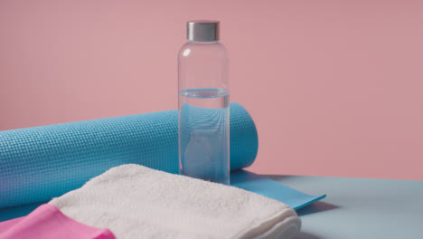 Fitness-Studio-Shot-Of-Water-Bottle-With-Exercise-Mat,-Resistance-Band-And-Towel-Against-Pink-Background