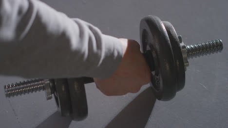 Close-Up-Studio-Fitness-Shot-Of-Hand-Picking-Up-Gym-Weight-On-Grey-Background-With-Shadow