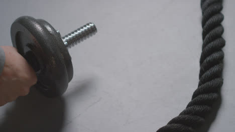Close-Up-Studio-Fitness-Shot-Of-Hand-Putting-Down-Gym-Weight-On-Grey-Background-With-Battle-Rope