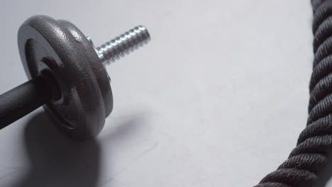 Close-Up-Studio-Fitness-Shot-Of-Hand-Picking-Up-Gym-Weight-On-Grey-Background-With-Battle-Rope