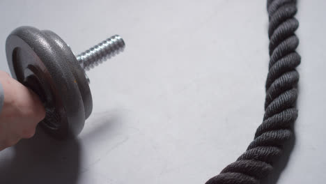 Close-Up-Studio-Fitness-Shot-Of-Hand-Putting-Down-Gym-Weight-On-Grey-Background-With-Battle-Rope