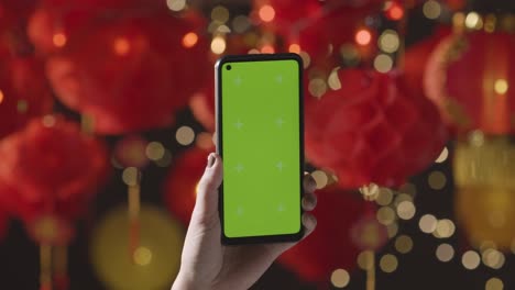 Hand-Holding-Green-Screen-Mobile-Phone-With-Chinese-Lanterns-Hung-In-Background-1