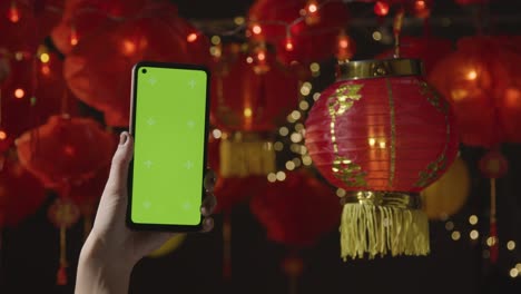 Hand,-Die-Ein-Greenscreen-Handy-Mit-Chinesischen-Laternen-Hält,-Die-Im-Hintergrund-Aufgehängt-Sind-2