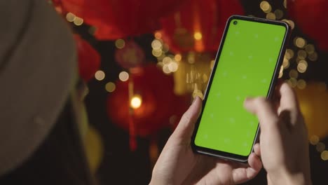 Woman-Using-Green-Screen-Mobile-Phone-With-Chinese-Lanterns-Hung-In-Background-