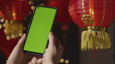Hand,-Die-Ein-Greenscreen-Handy-Mit-Chinesischen-Laternen-Hält,-Die-Im-Hintergrund-Aufgehängt-Sind-3