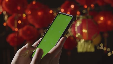 Woman-Using-Green-Screen-Mobile-Phone-With-Chinese-Lanterns-Hung-In-Background-1