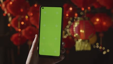 Hand-Holding-Green-Screen-Mobile-Phone-With-Chinese-Lanterns-Hung-In-Background-4