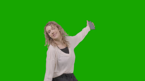 Studio-Shot-Of-Young-Woman-Listening-To-Music-On-Mobile-Phone-And-Dancing-Against-Green-Screen-4