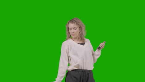 Studio-Shot-Of-Young-Woman-Listening-To-Music-On-Mobile-Phone-And-Dancing-Against-Green-Screen-5